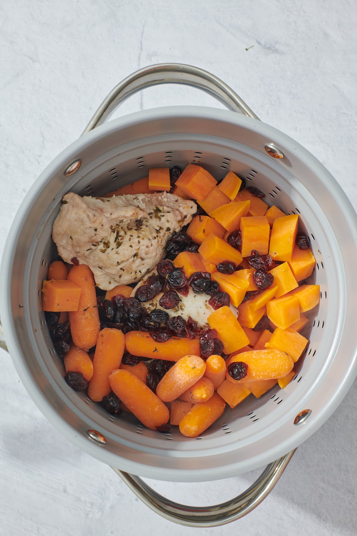 Turkey breast, baby carrots, cranberries, and peeled and diced sweet potatoes in steamer pot.