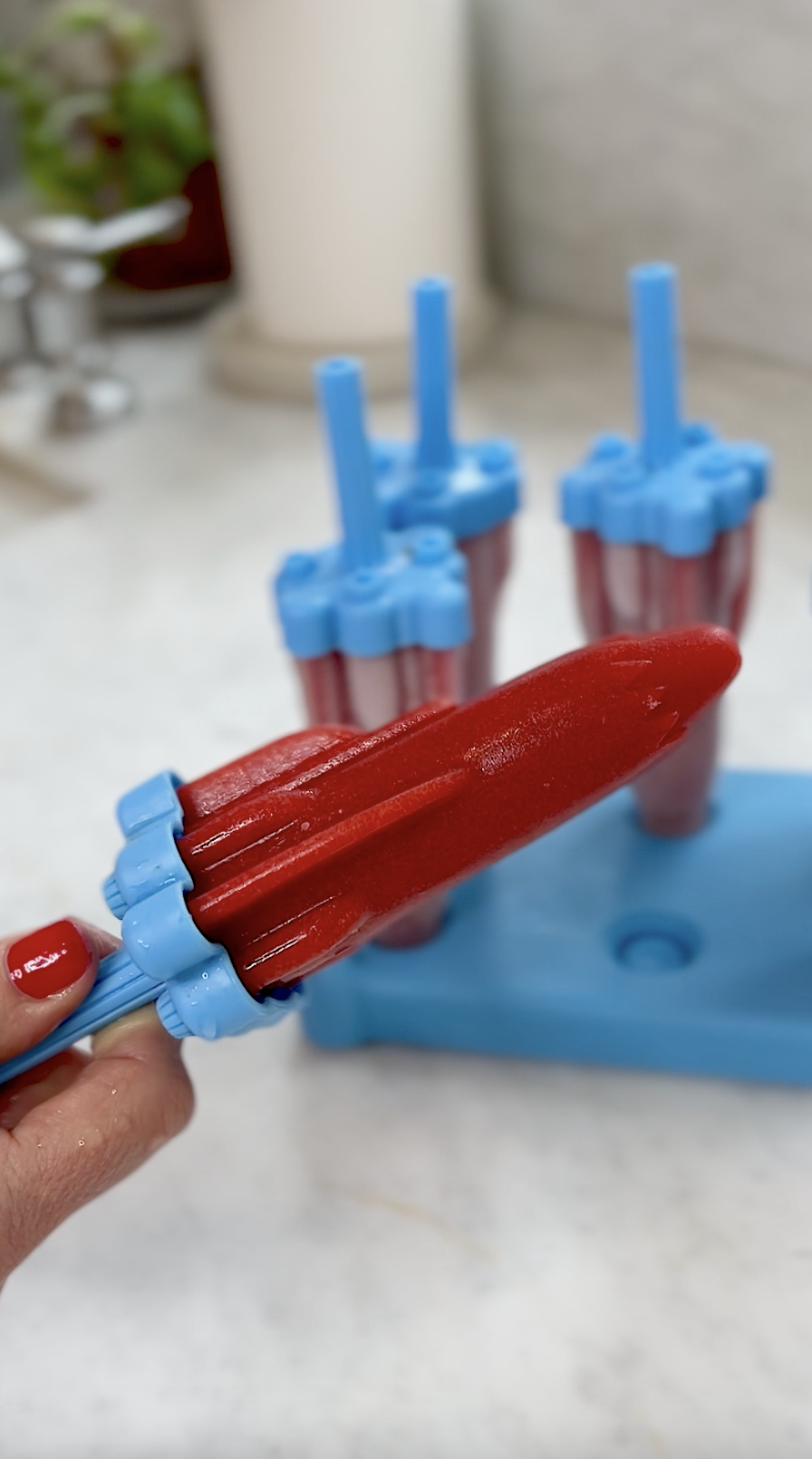 Hand holding strawberry popsicle.