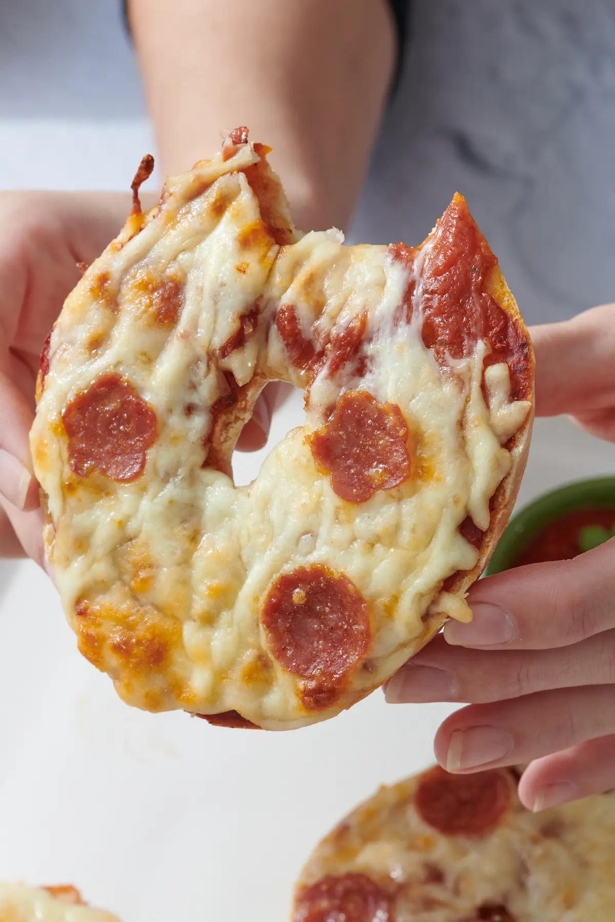 hands holding pizza bagel with bite taken out