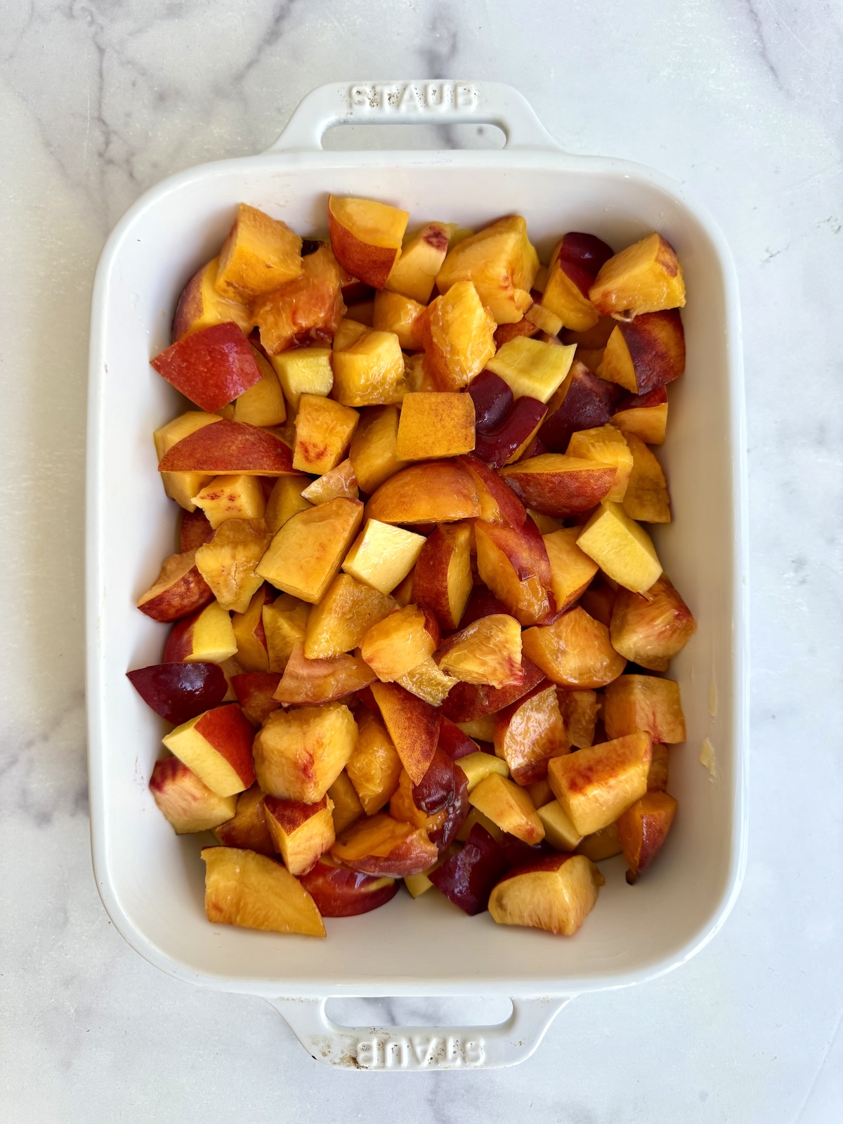 Chopped peaches spread in a white baking dish before adding the crumble topping.