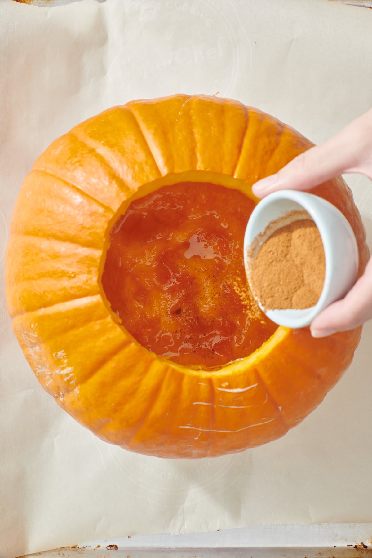 Pouring cinnamon into maple syrup coated inside of pumpkin.