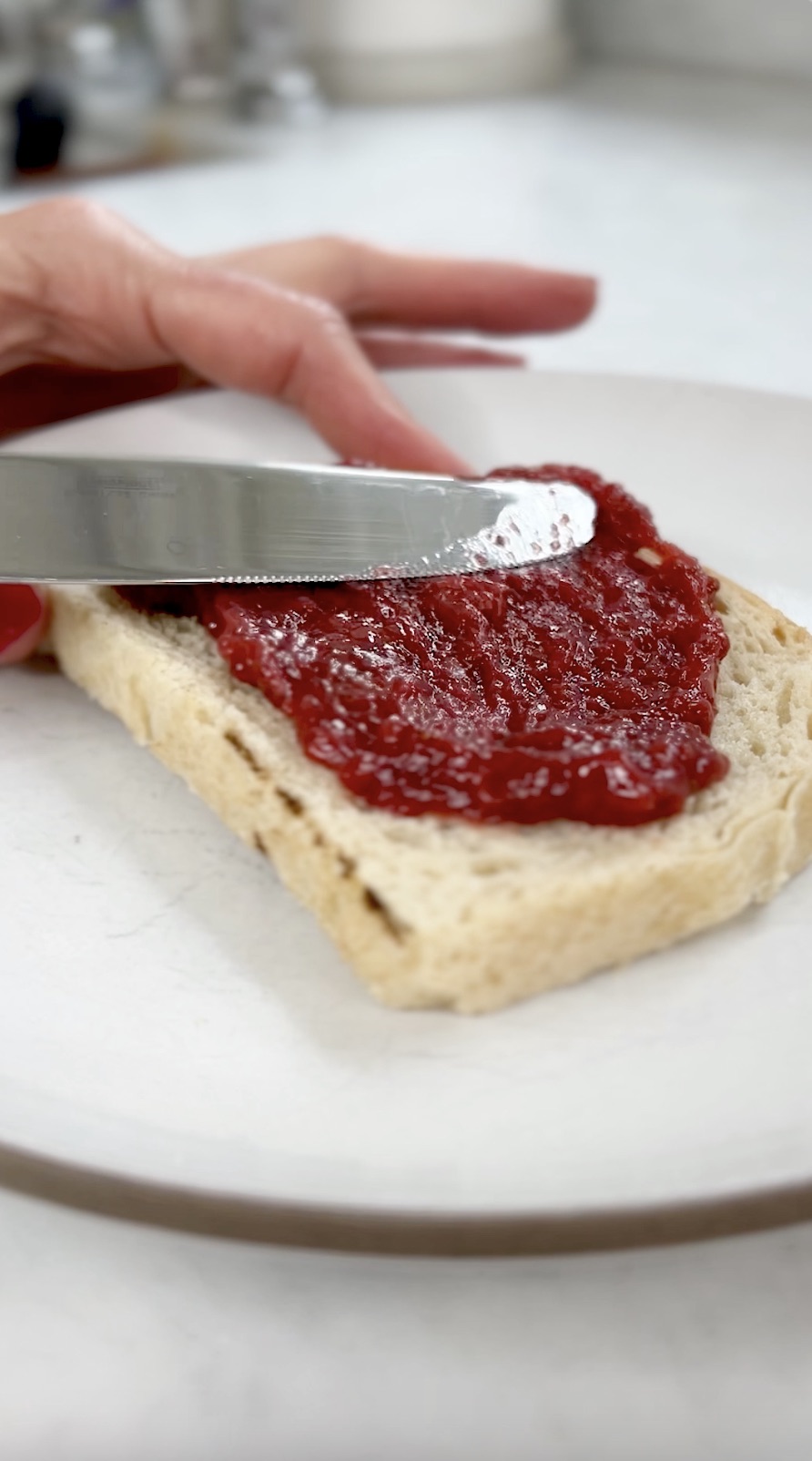 Knife spreading preserves on a piece of toast.