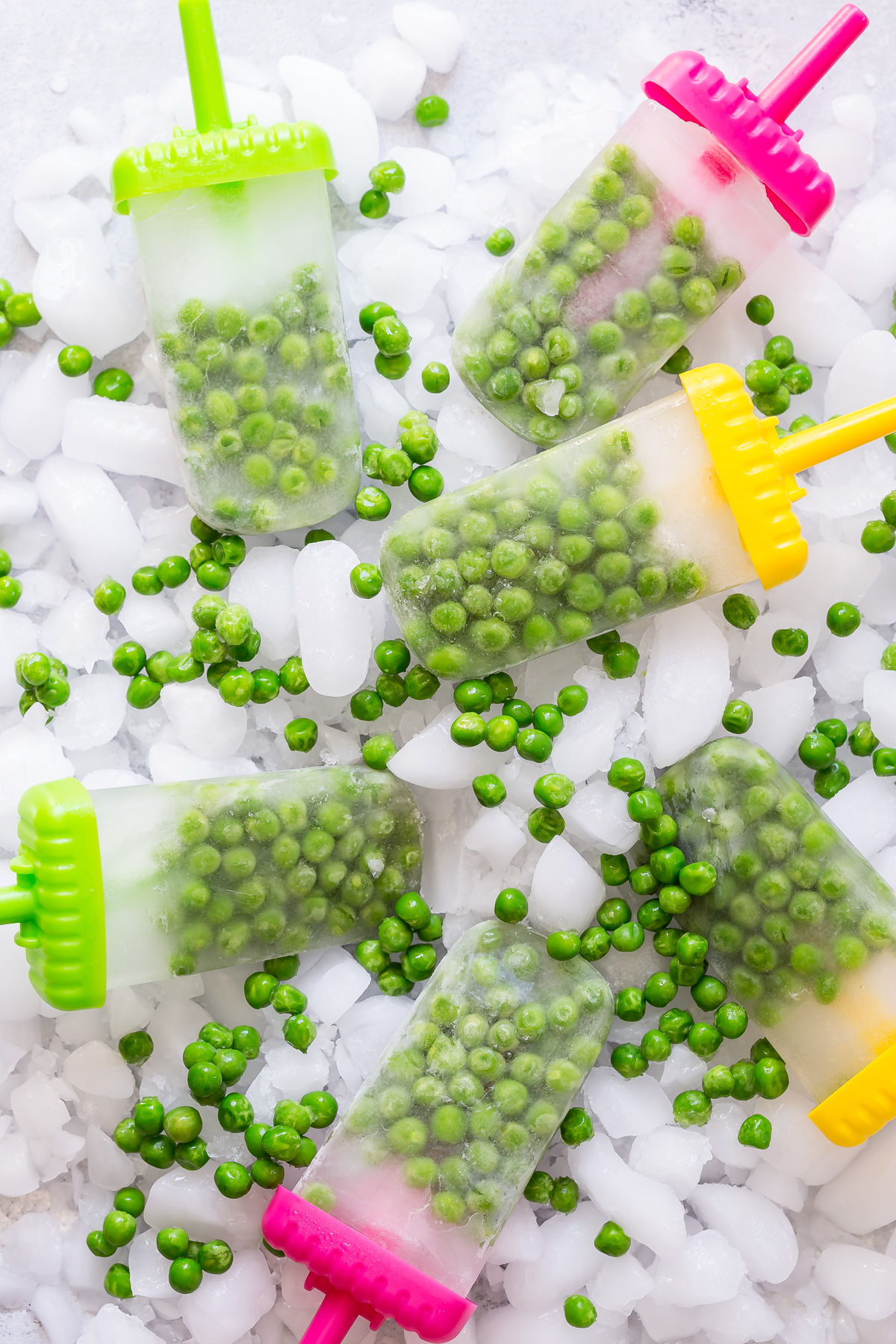 Frozen pea popsicles with whole green peas suspended in ice, scattered with loose peas and crushed ice.