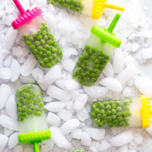 Green pea popsicles on colorful sticks arranged on crushed ice.
