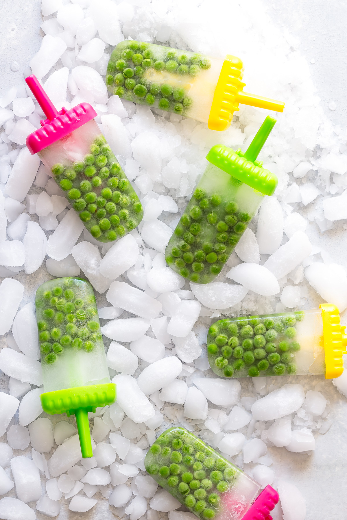 Green pea popsicles on colorful sticks arranged on crushed ice.