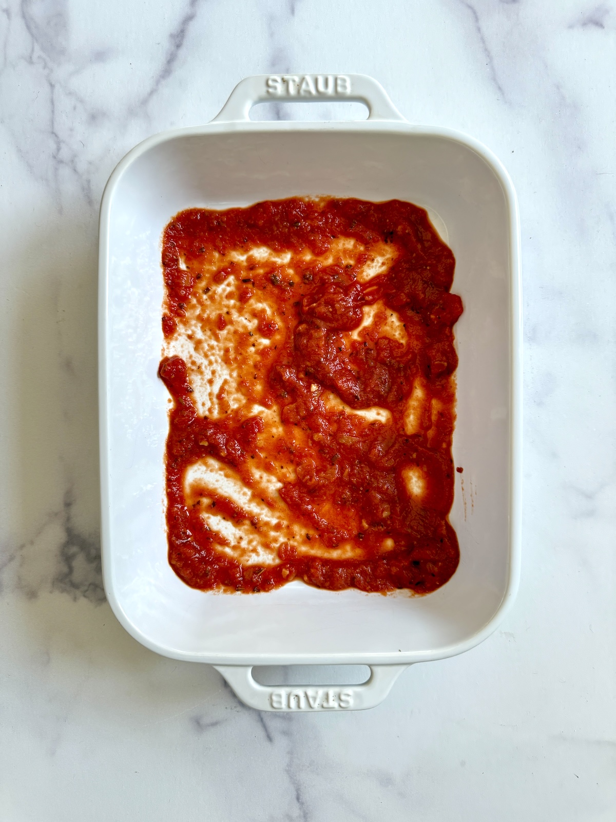Marinara sauce coating the bottom of a baking dish.