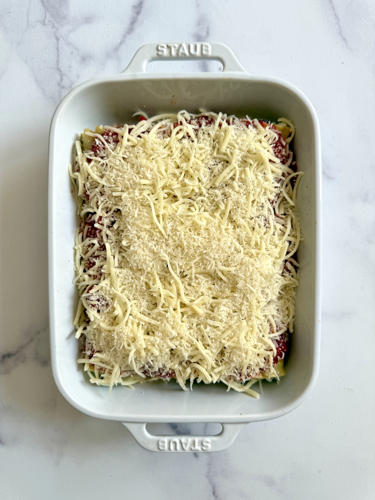 Lasagna rolls topped with cheese and ready to bake.