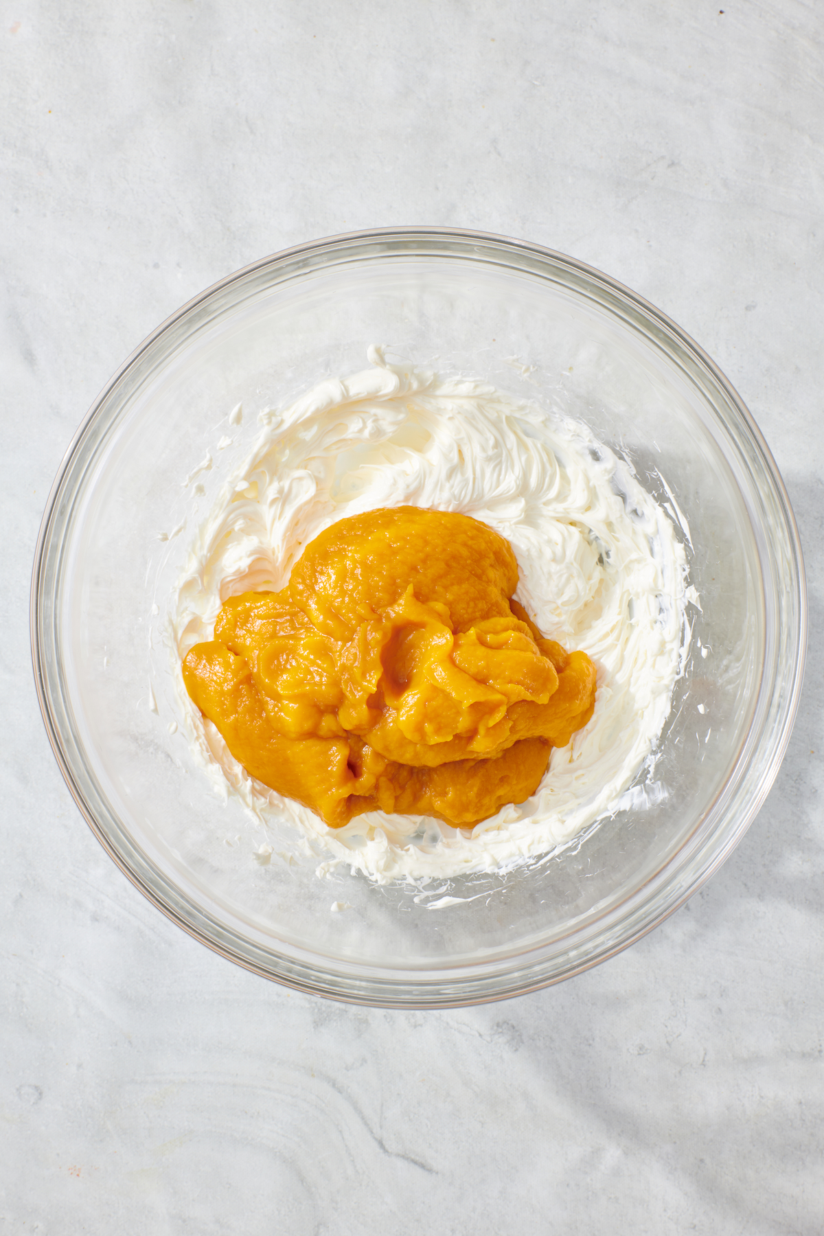 Whipped cream cheese and pumpkin puree in mixing bowl before being combined.
