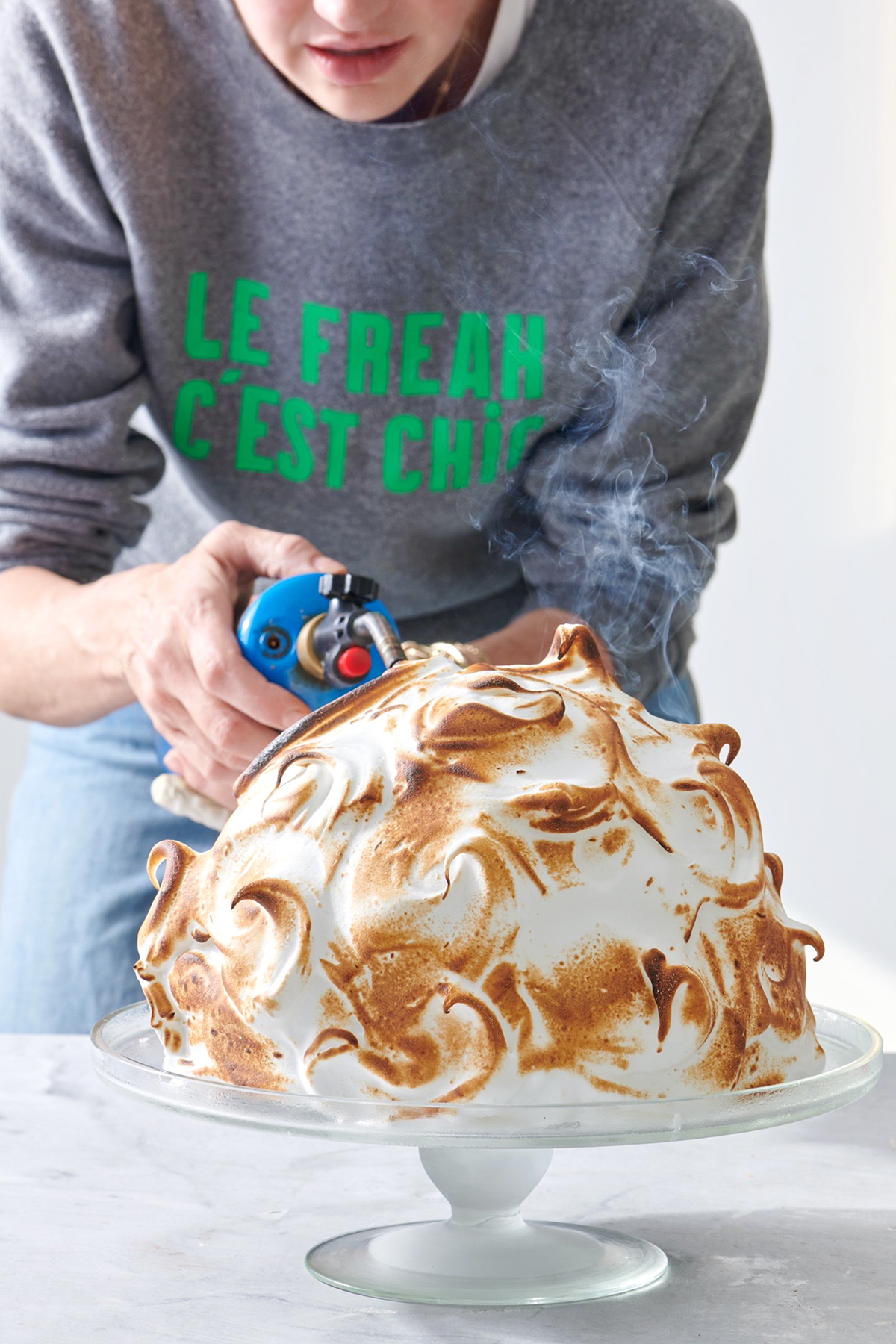 A person using a blow torch to toast meringue on the outside of a baked Alaska.