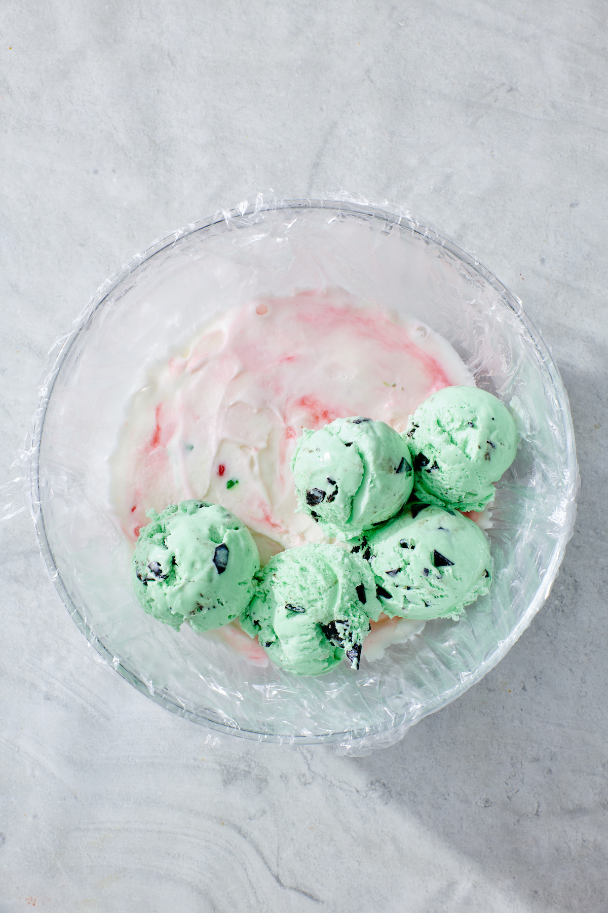 Scoops of mint chocolate chip ice cream on top of peppermint ice cream before smoothing into a layer.