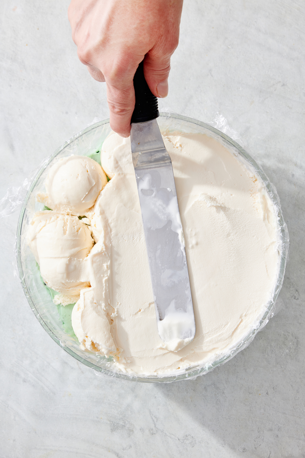 Smoothing vanilla ice cream on top of other layers of ice cream in a bowl.