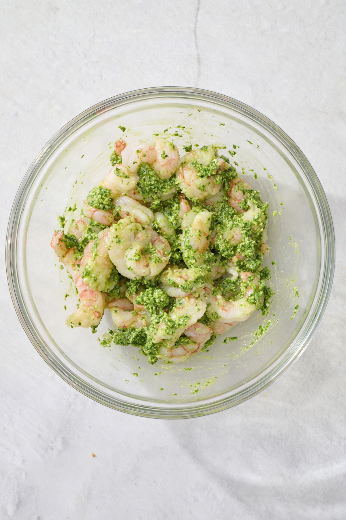 Raw shrimp in mixing bowl with pesto.