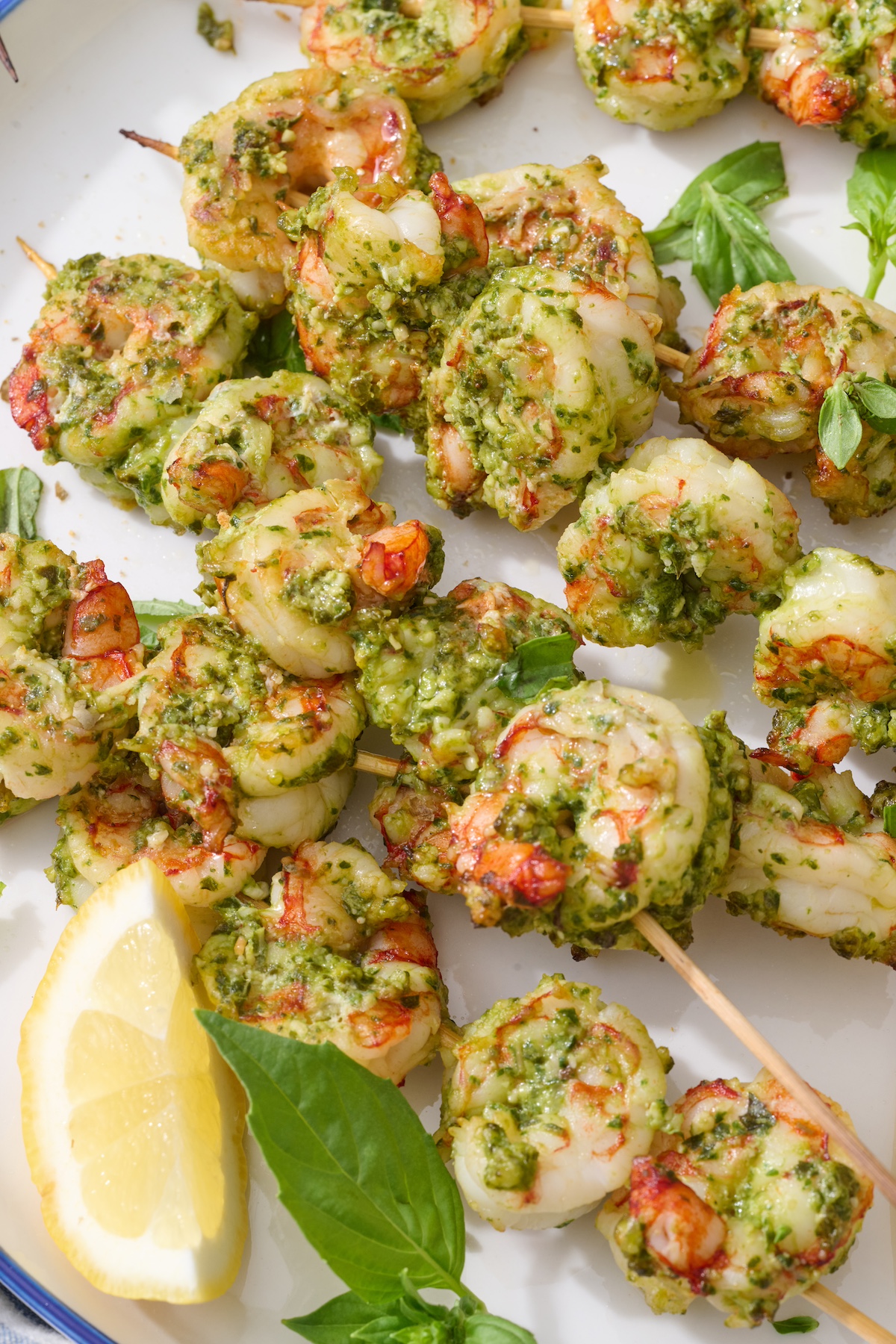 Pesto shrimp skewers served on plate with lemon wedges.