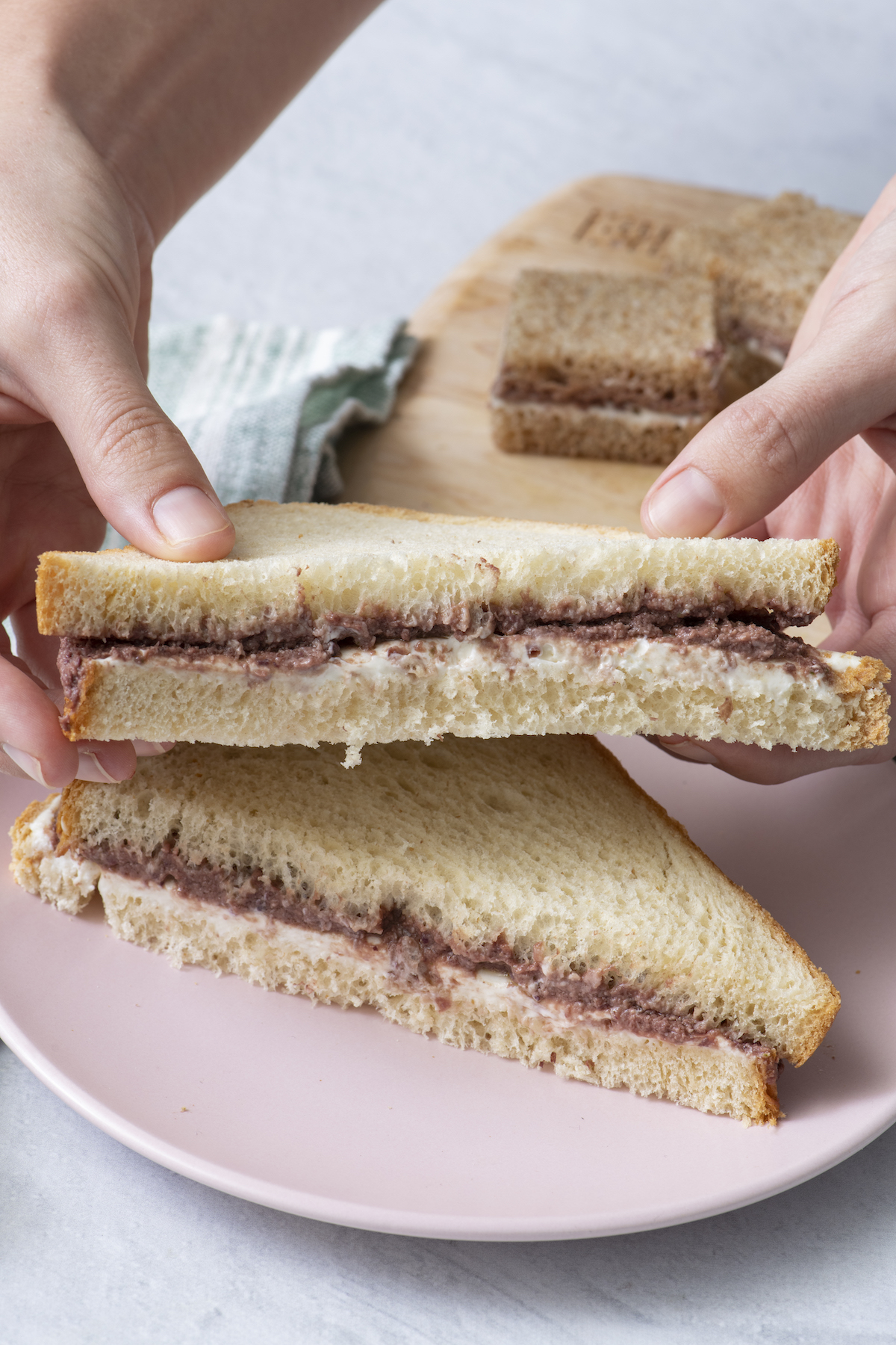 Hands holding olive tapenade and cream cheese sandwich.