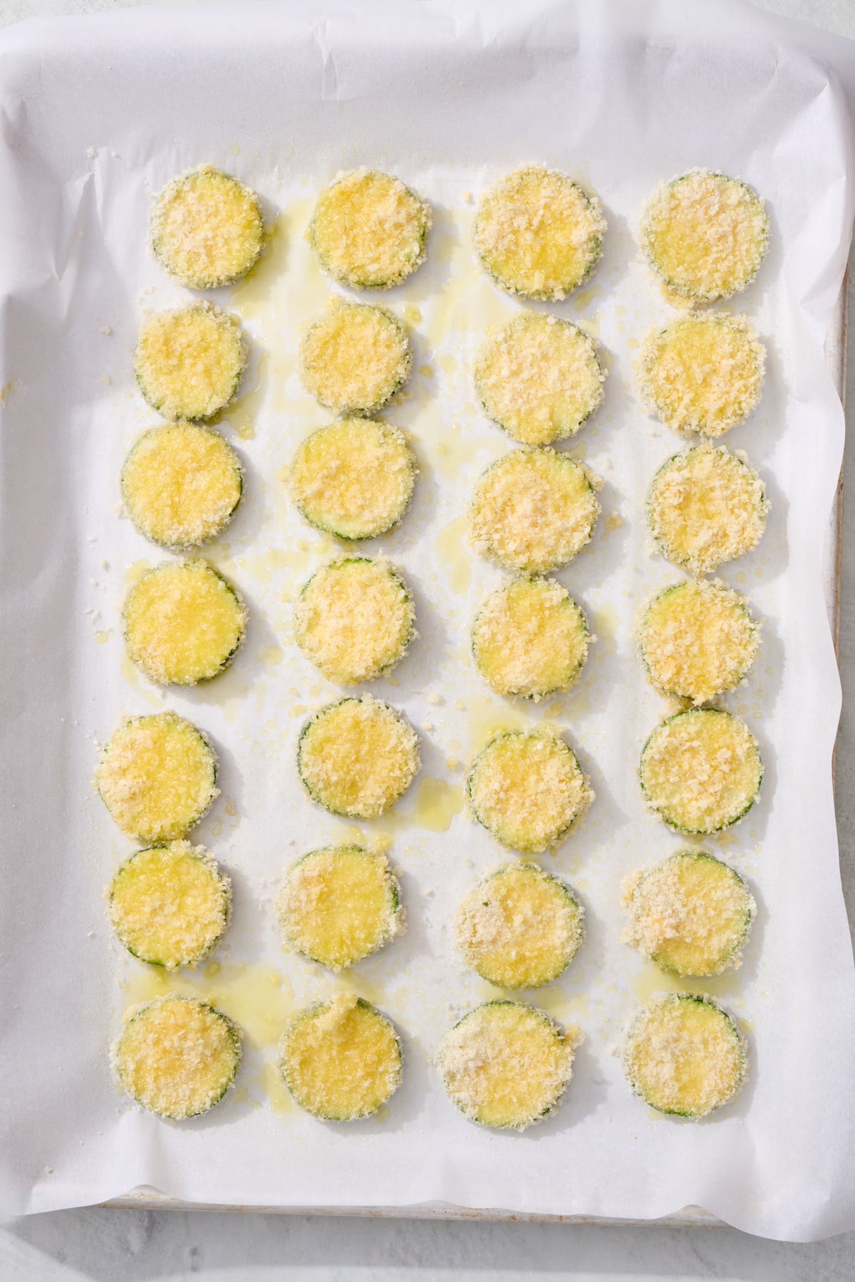 Breaded zucchini coins on baking sheet.