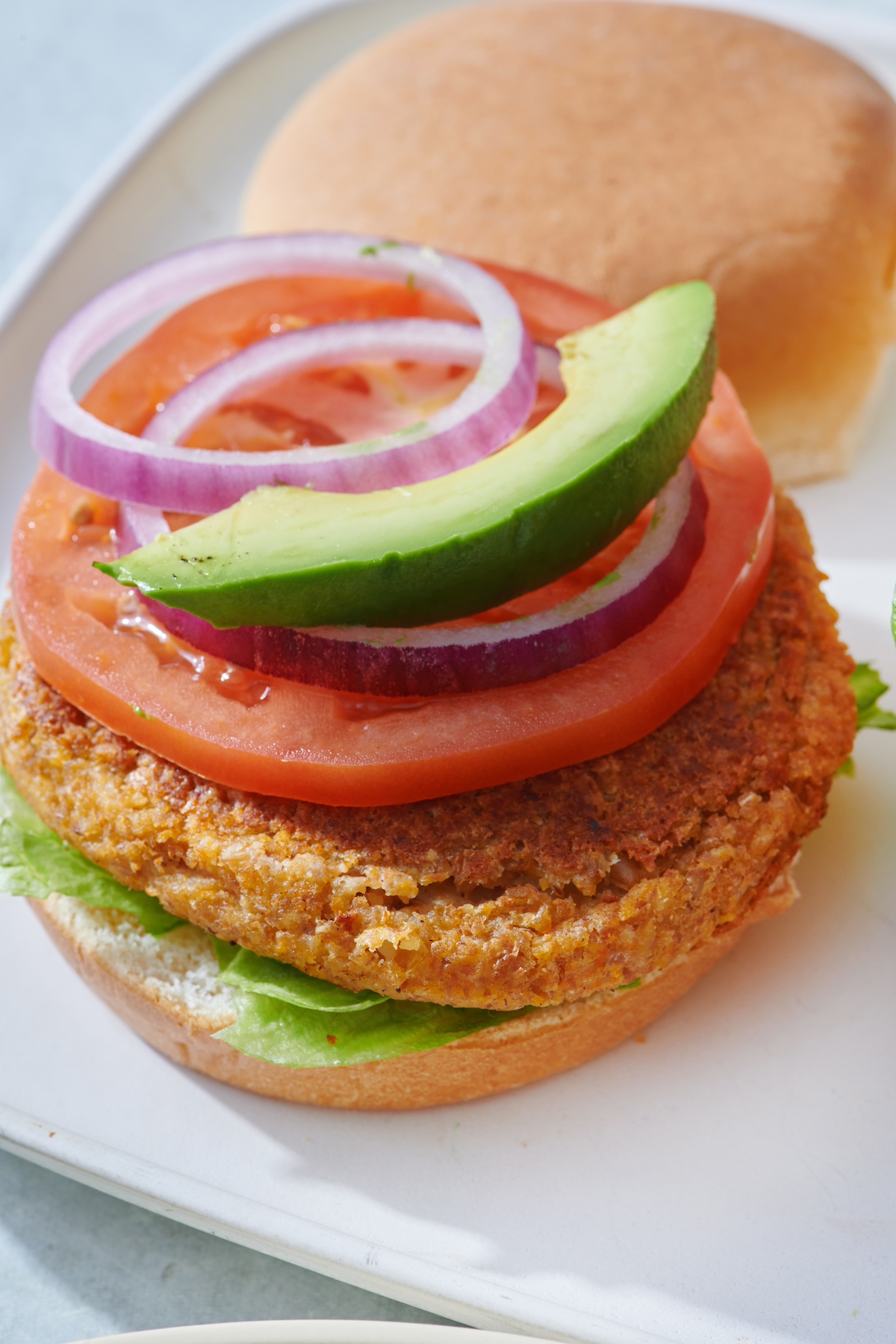 Veggie burger on bun topped with lettuce, tomato, onion and avocado.