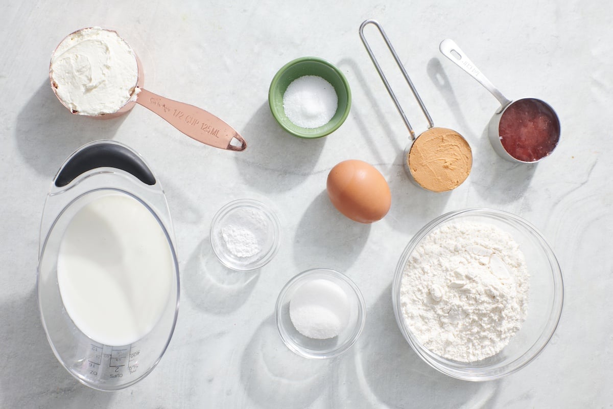 Ingredients for breakfast cupcakes. From top left going clockwise: cream cheese, baking powder, egg, peanut butter, jam, flour, sugar, salt and milk.