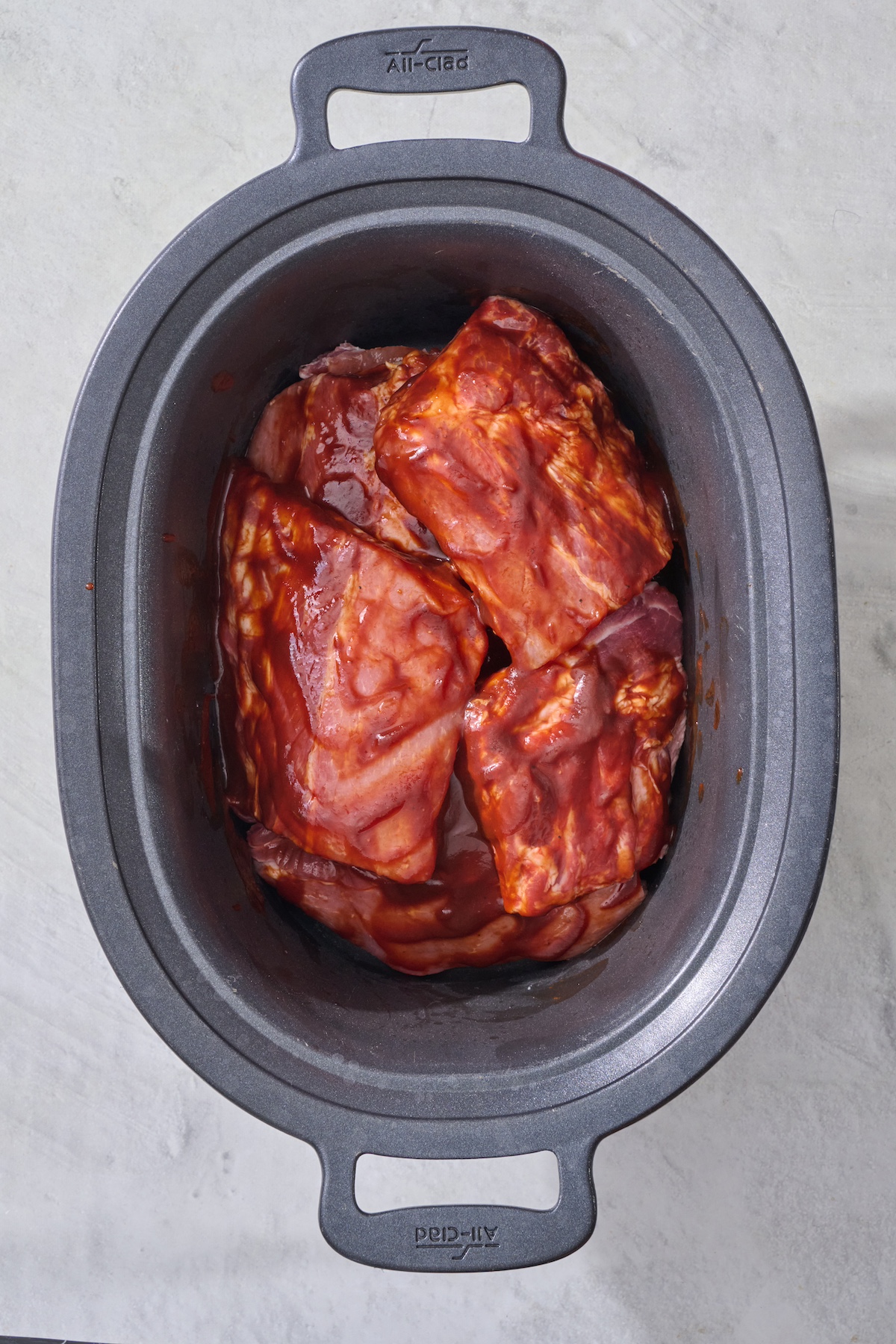 Ribs in crock pot with BBQ sauce before cooking.