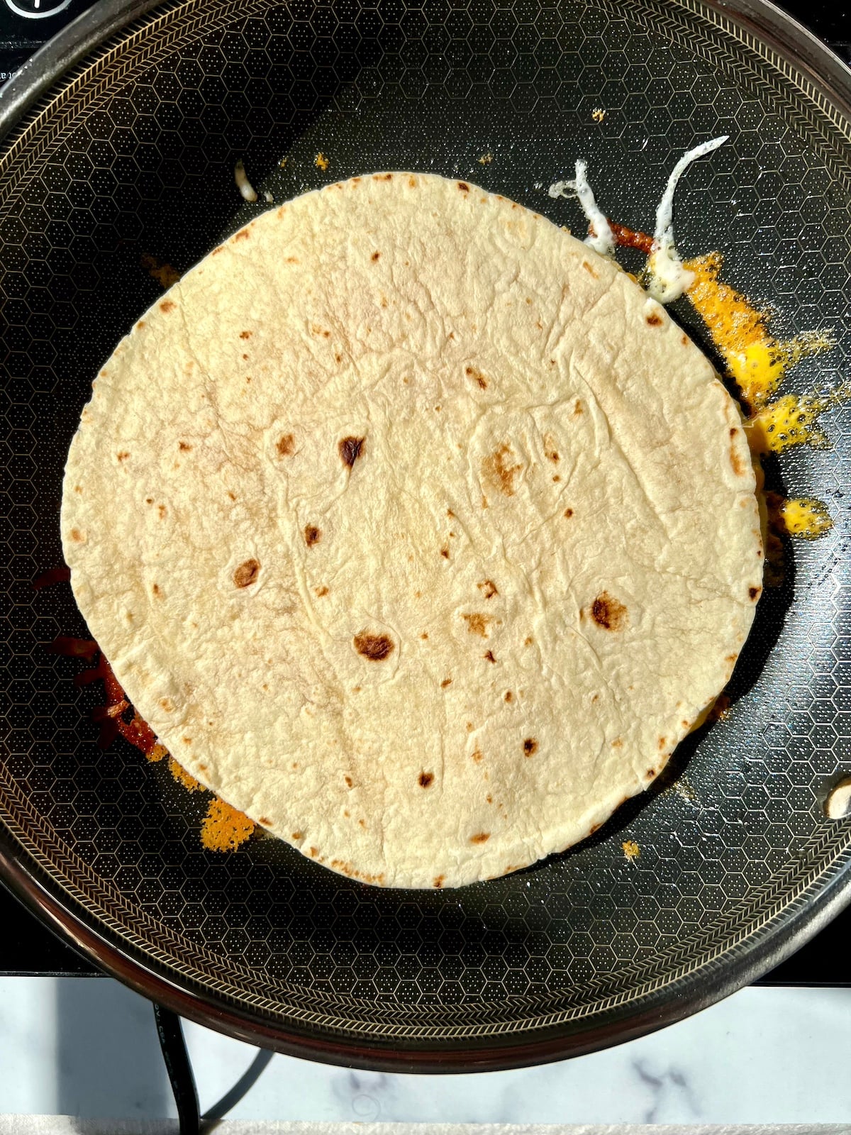 Tortilla on top of egg in pan.