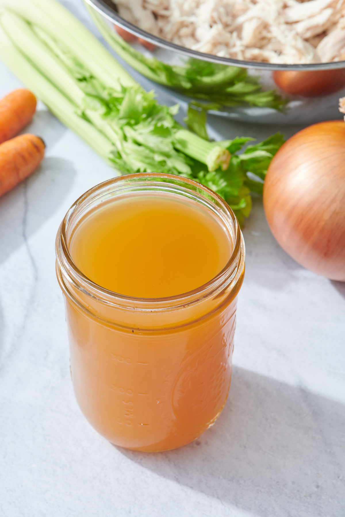 Chicken Stock in mason jar with ingredients in background.