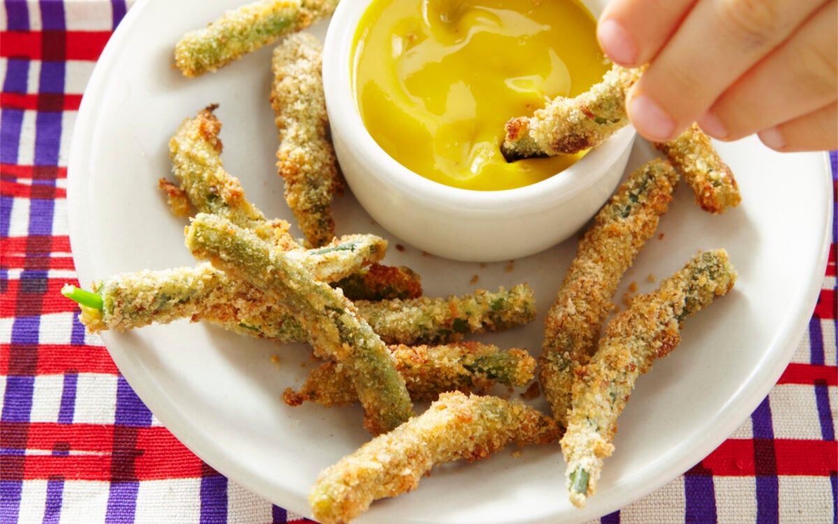 Green bean fries being dipped in honey mustard.