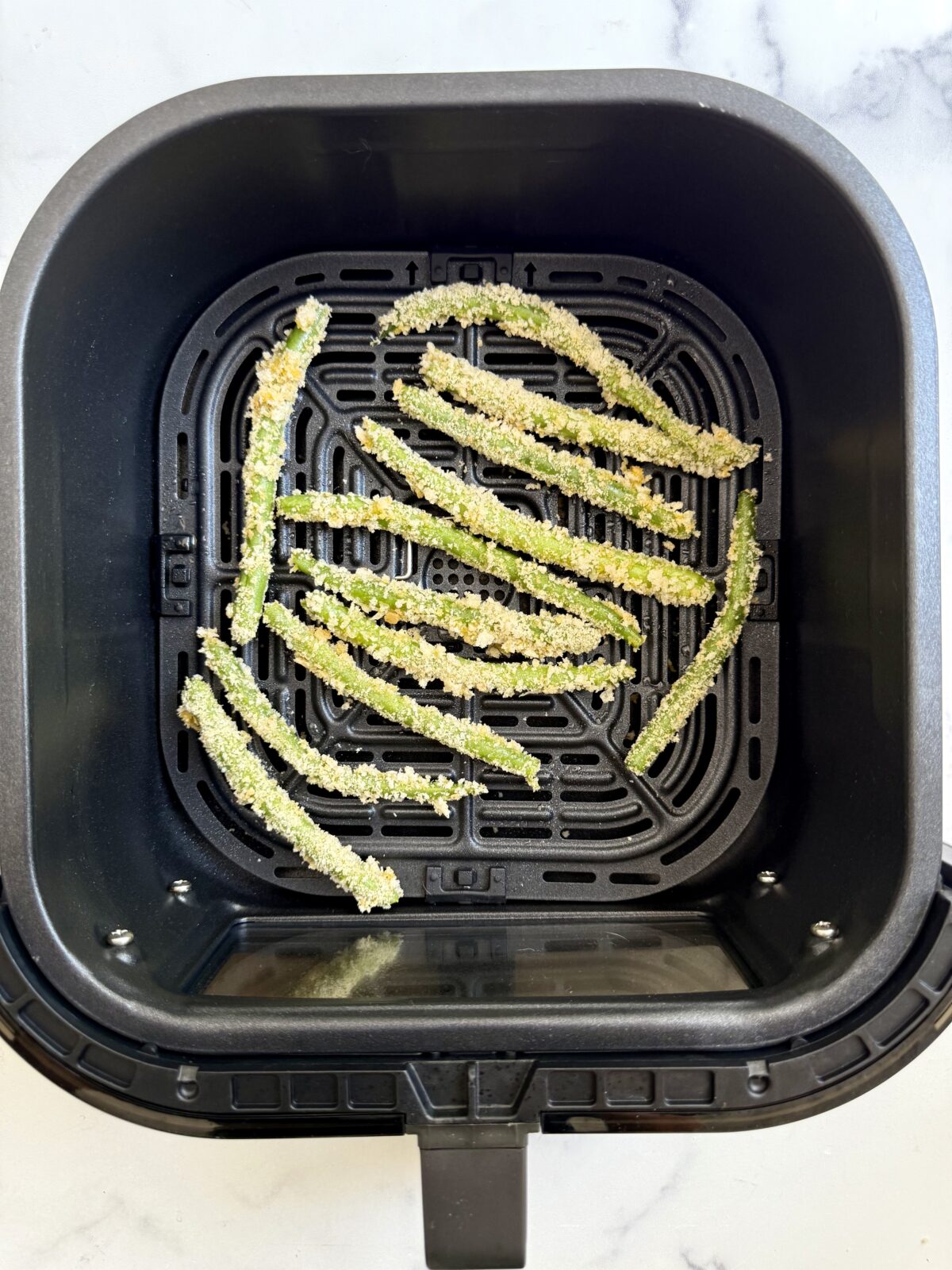 Breaded green beans in an air fryer basket.