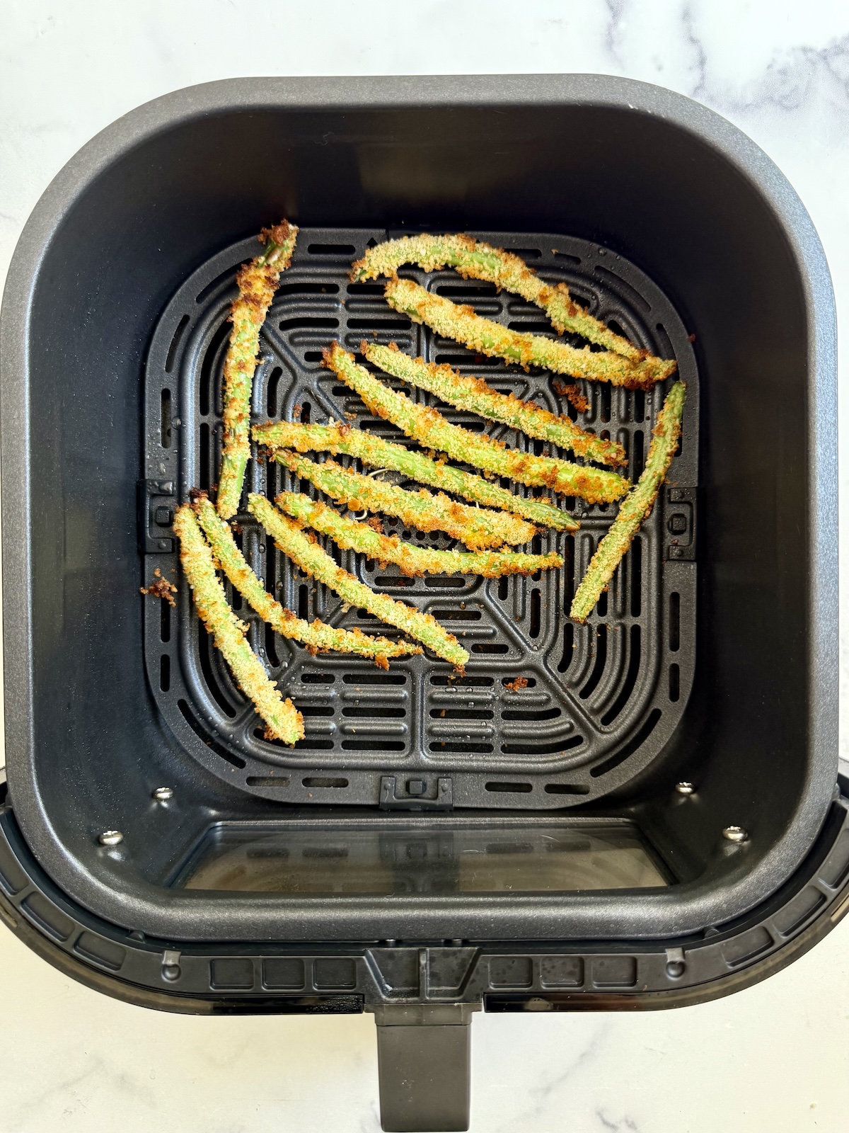 Cooked green bean fries in air fryer basket.