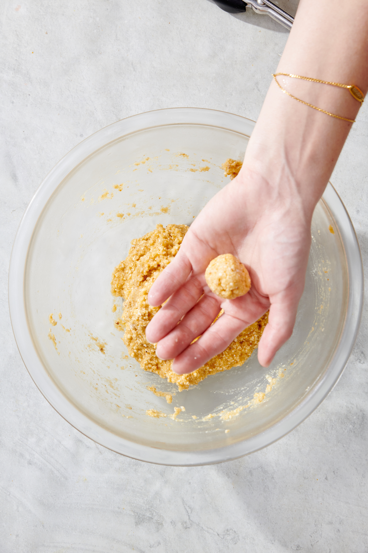 Hand holding one mini matzah ball above bowl of matzah ball mixture.