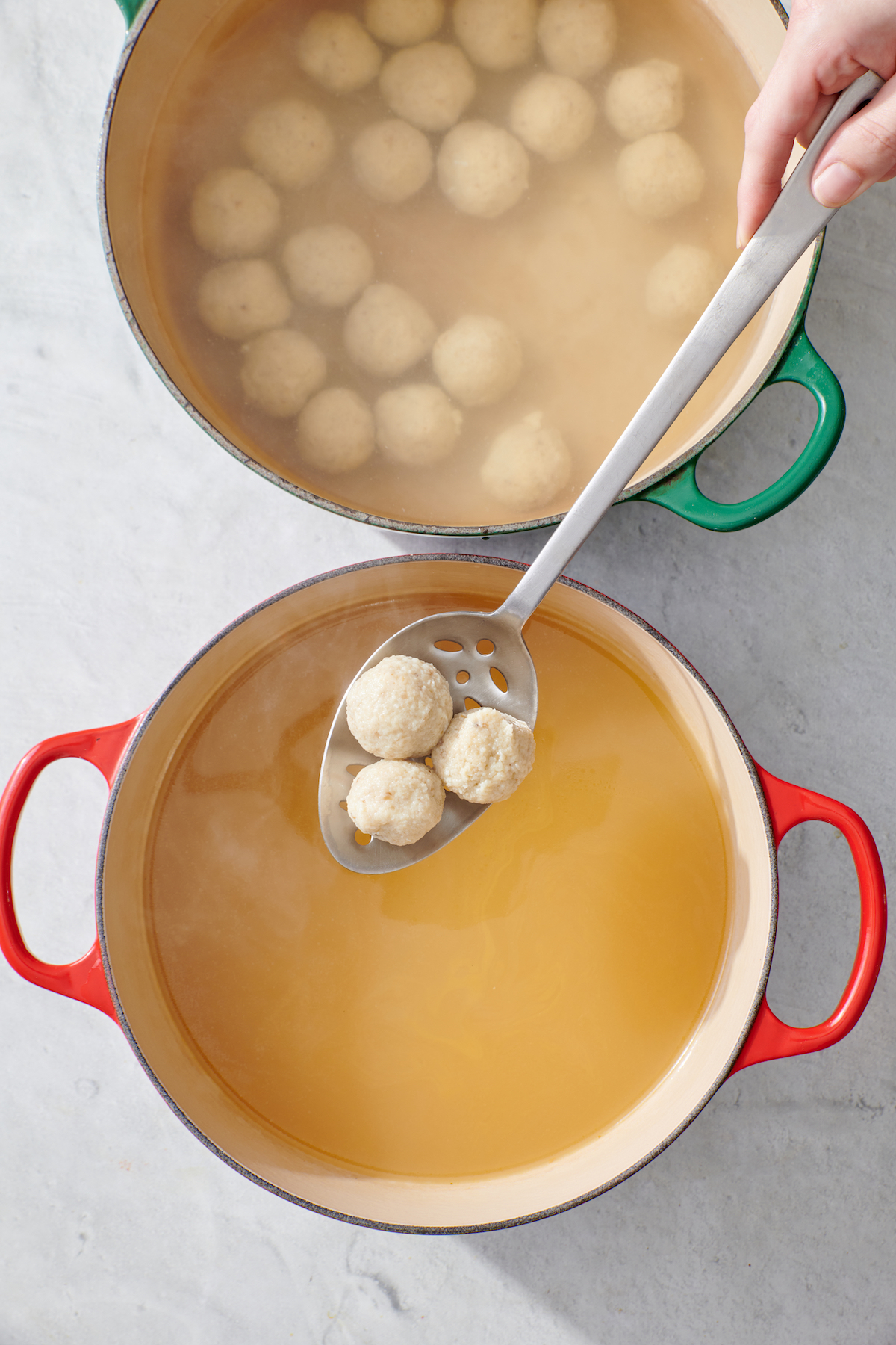 Spooning matzah balls from water into chicken stock.
