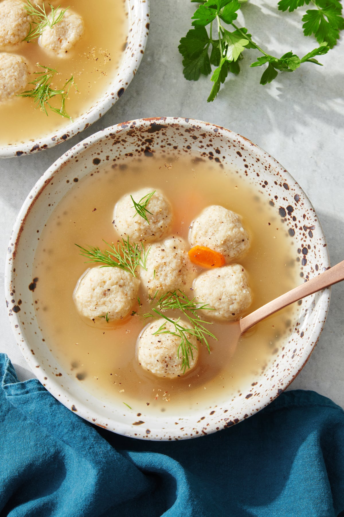 Mini matzah ball soup in bowl topped with dill.