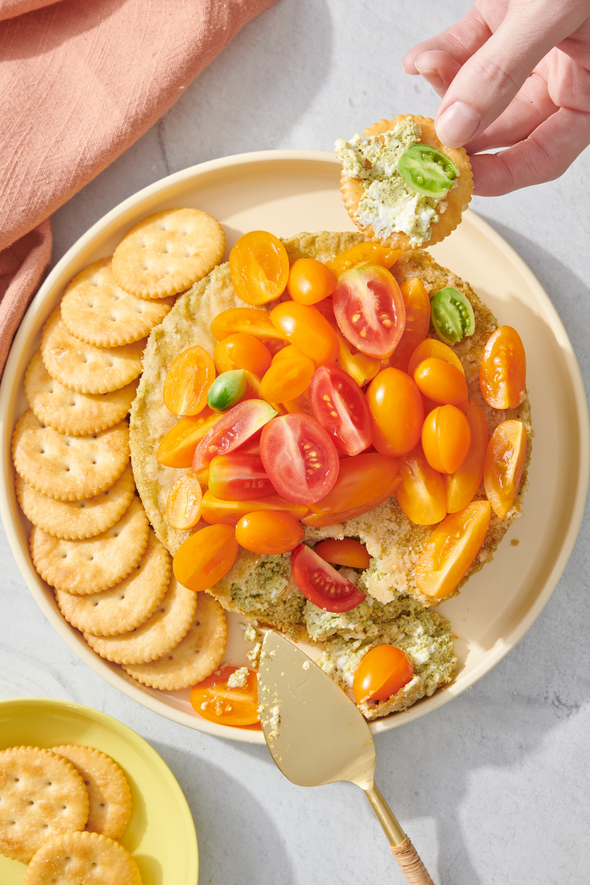 Hand taking a scoop of basil pesto cheesecake dip on a cracker.