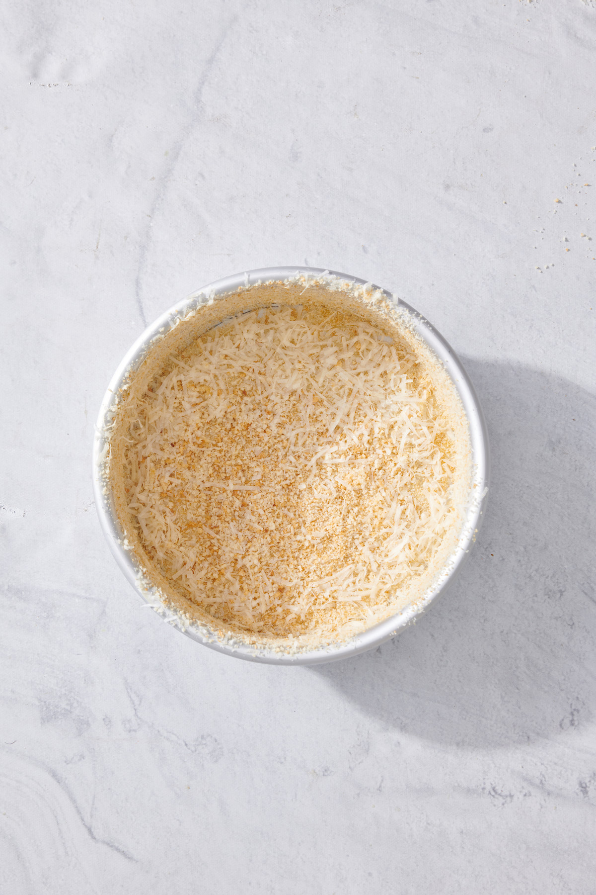 Small cake pan coated with breadcrumb and parmesan cheese mixture.