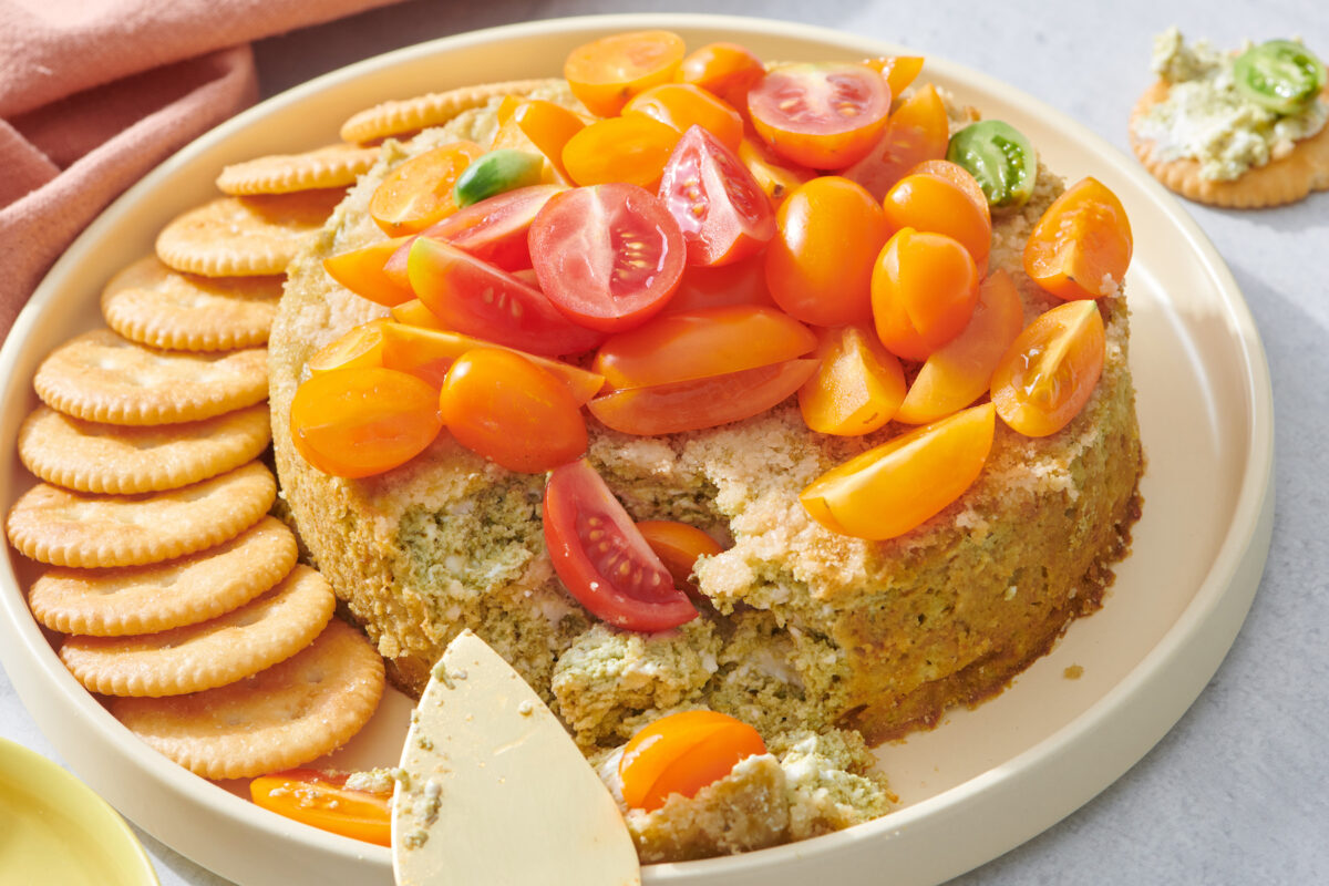 Platter with savory basil pesto cheesecake dip and crackers for serving.