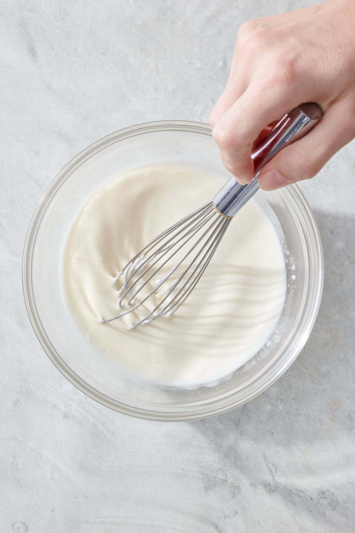 A hand whisking Waldorf Salad dressing.