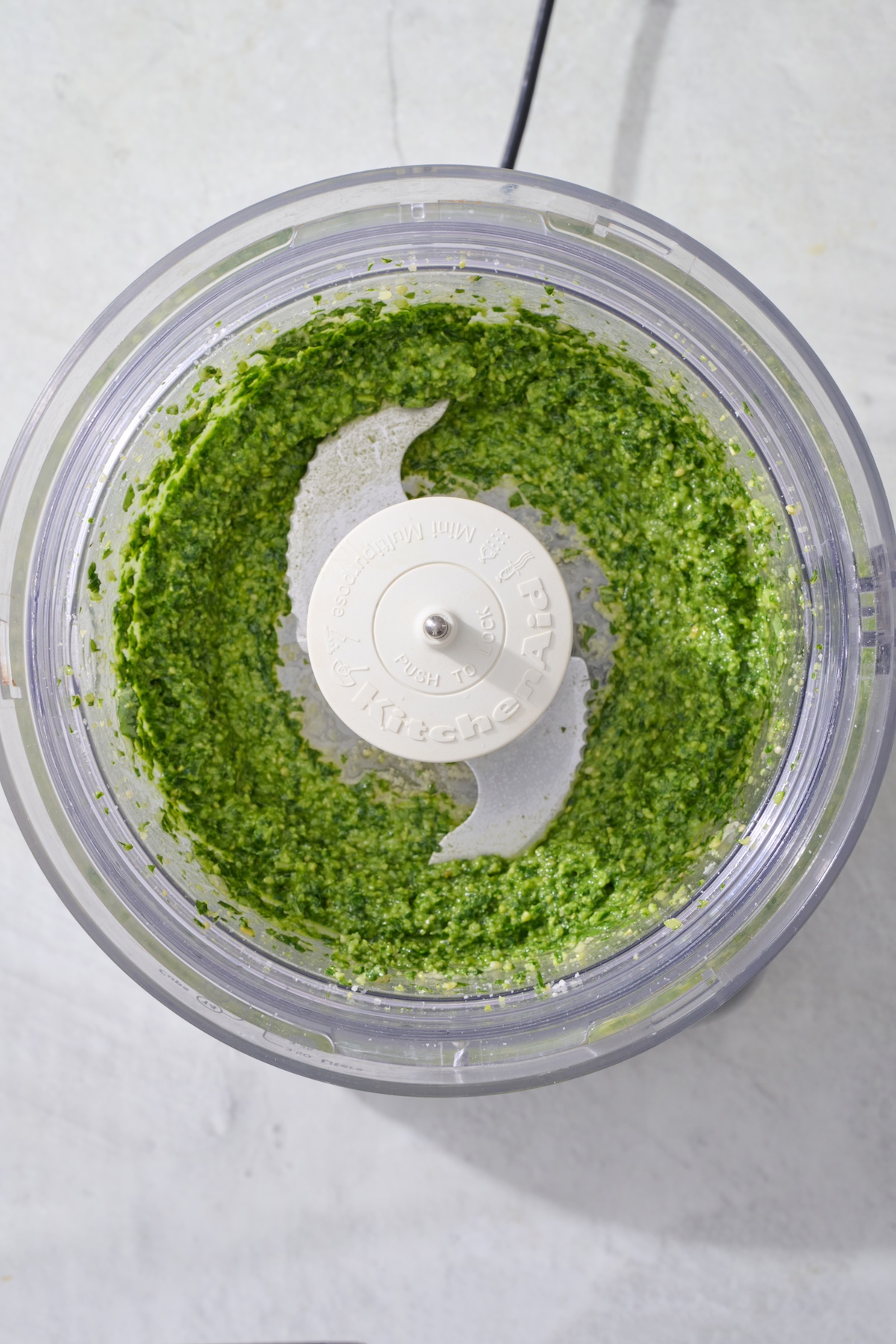 Pureed basil pesto ingredients in food processor.
