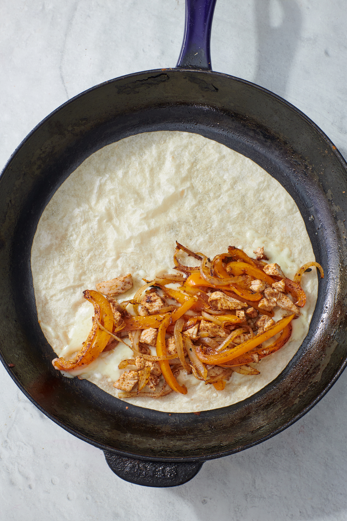 tortilla on frying pan with chicken fajita mixture and cheese.