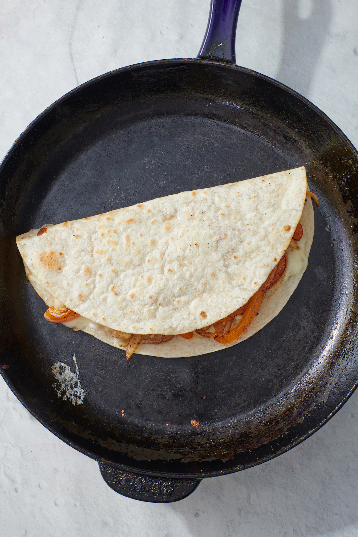 Folded chicken fajita quesadilla on frying pan.