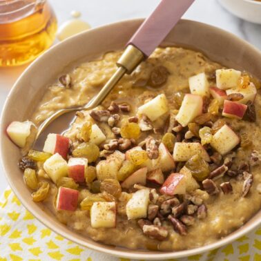 Pumpkin spice oatmeal in a bowl topped with chopped apples, raisins and walnuts.