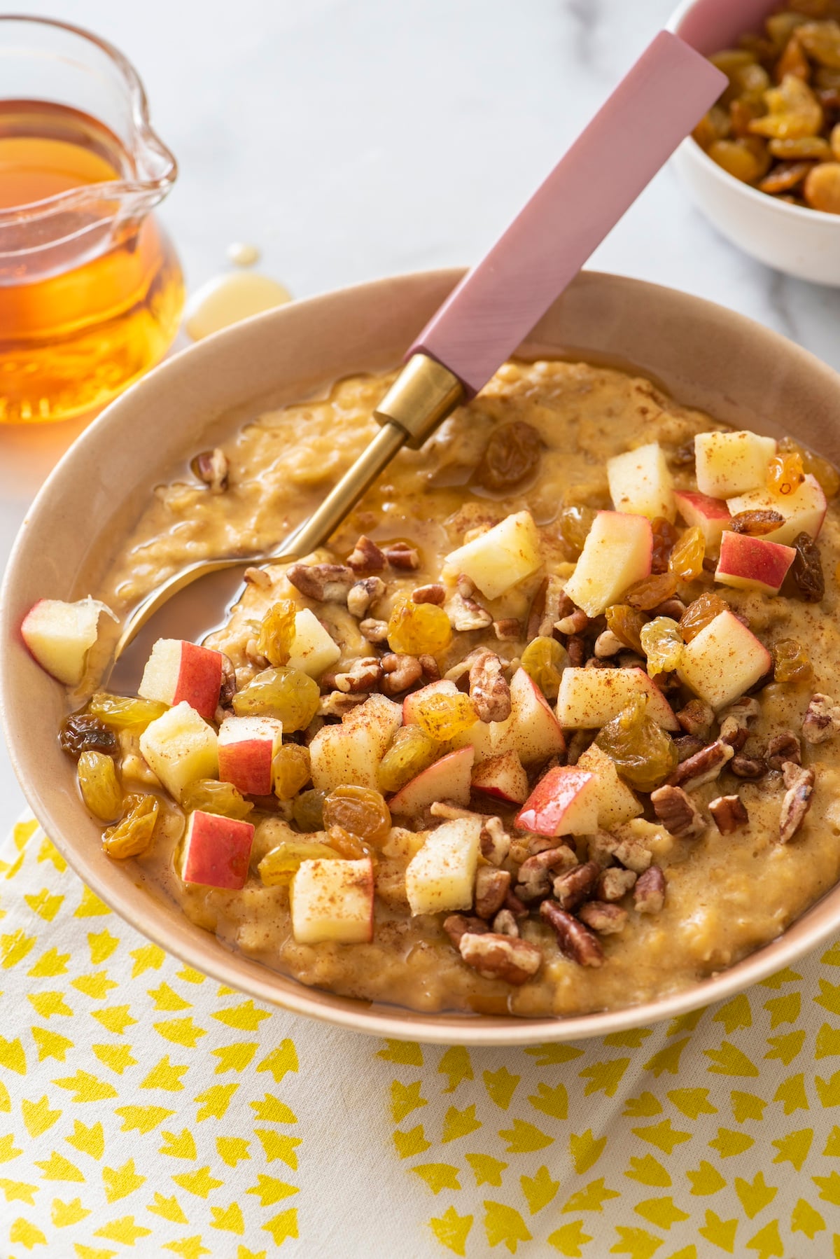 Pumpkin spice oatmeal in a bowl topped with chopped apples, raisins and walnuts.