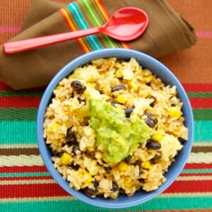 Mexican fried rice with black beans, corn, and guacamole served in a blue bowl.
