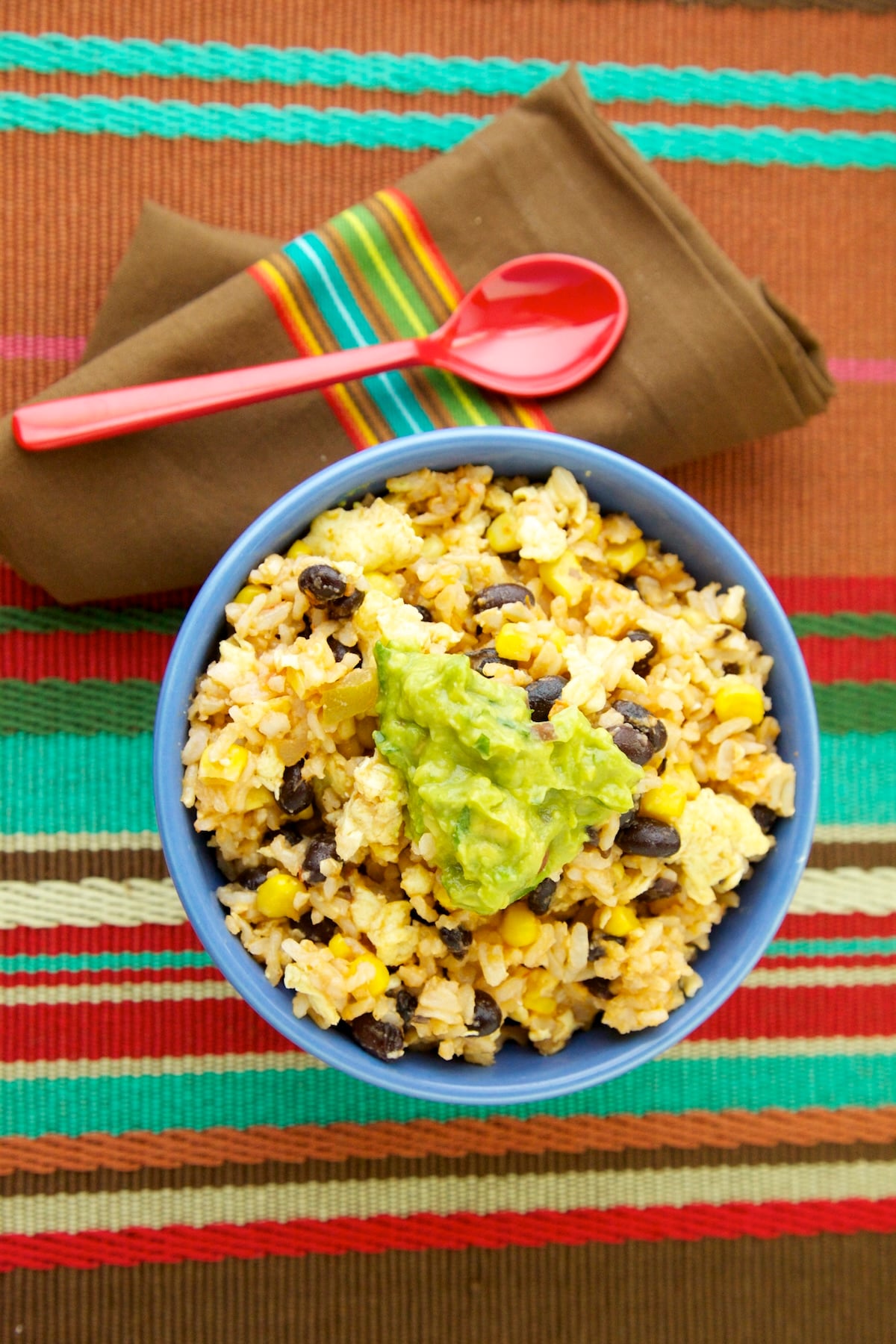Mexican fried rice with black beans, corn, and guacamole served in a blue bowl.