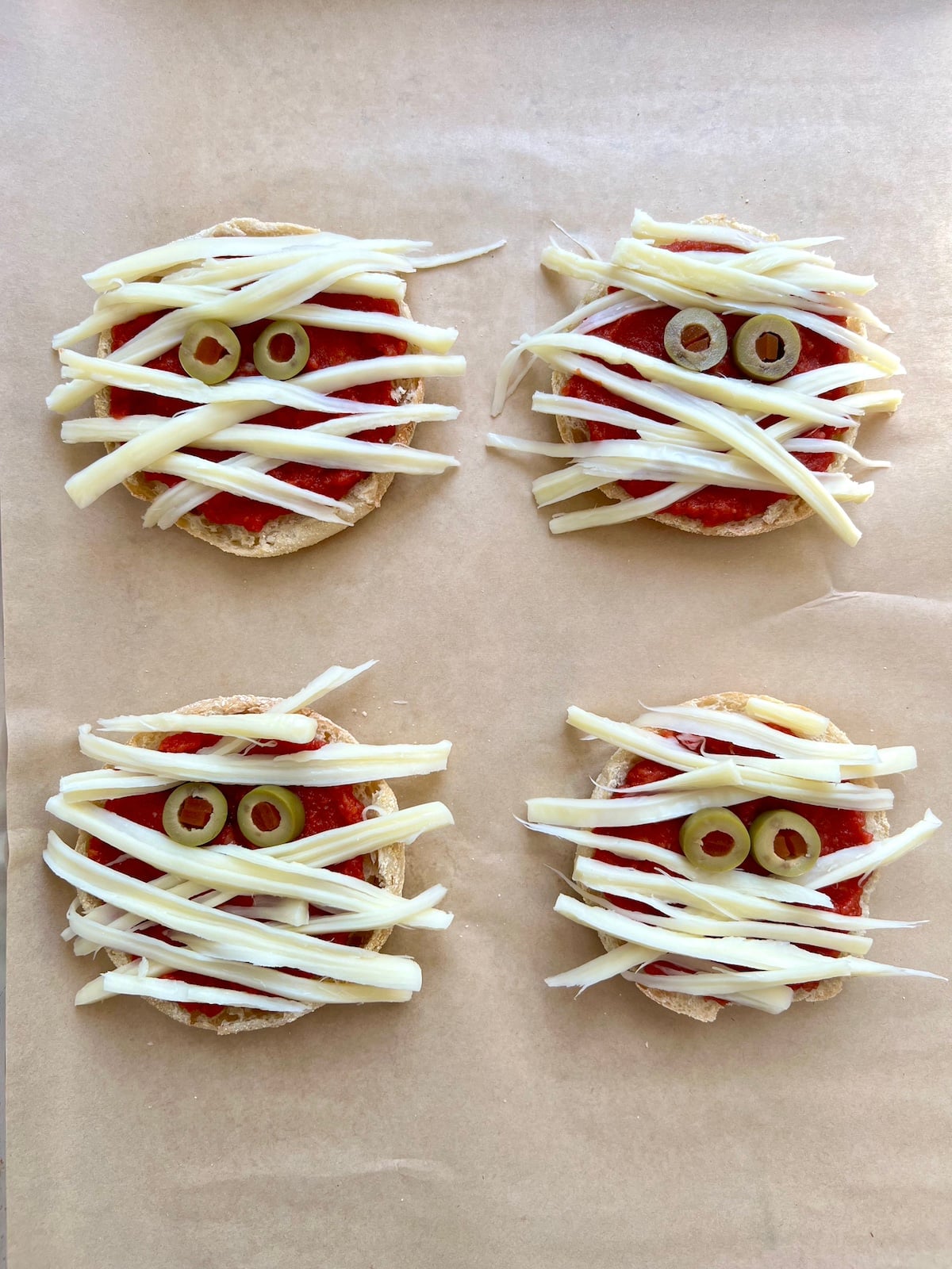 Pizza mummies on baking sheet ready to be baked.