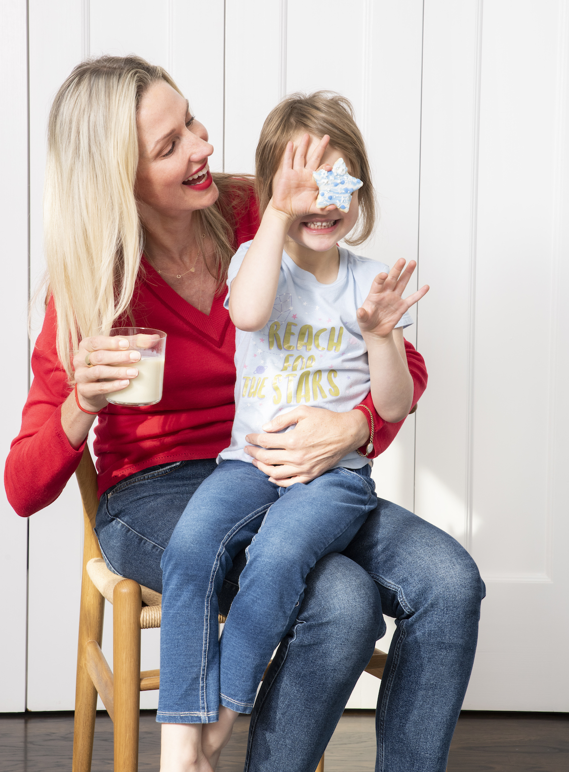 Kids holding a cookie in front of her face while sitting in mother's lap.