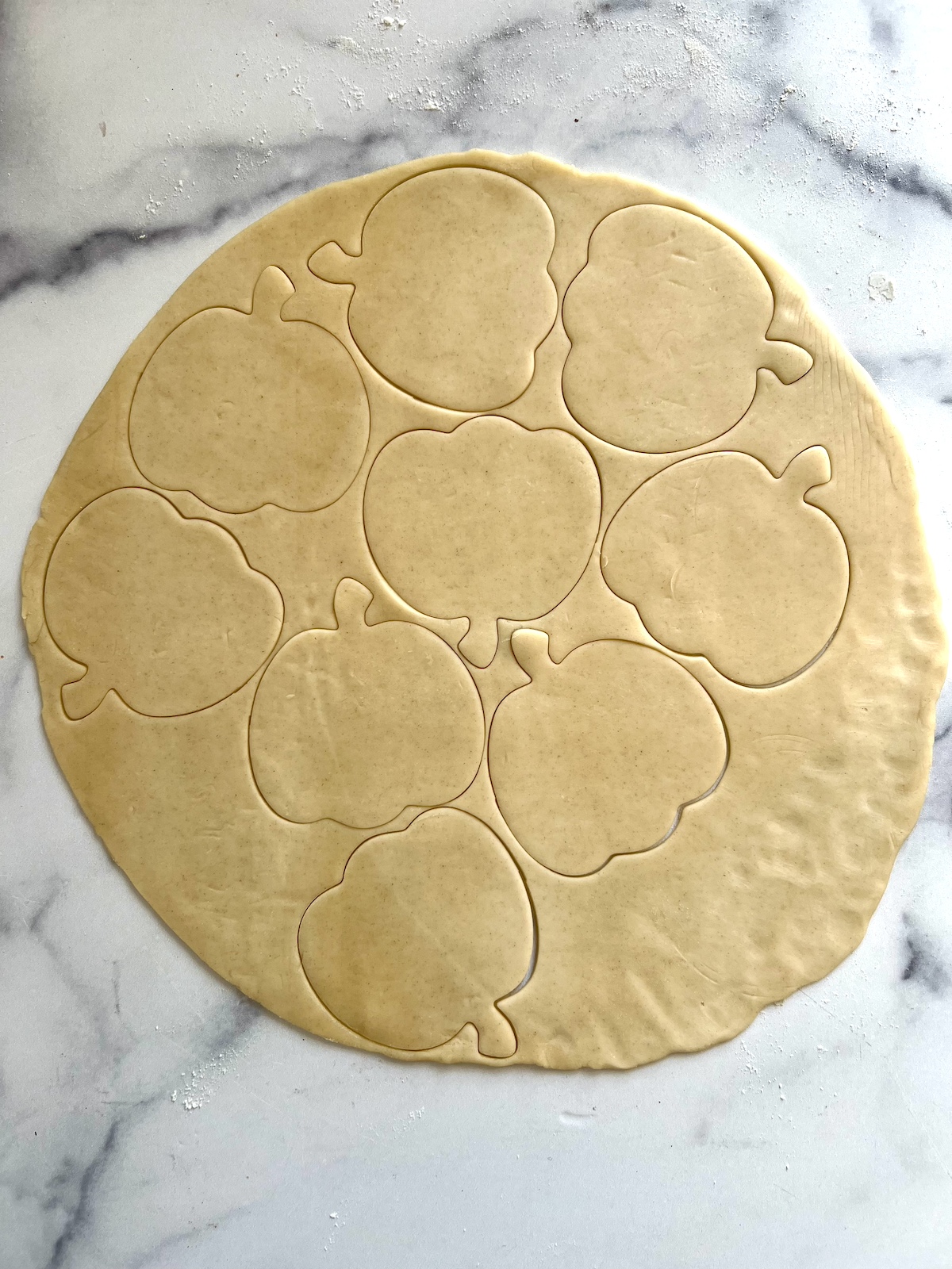 Pie dough rolled out on a floured surface with pumpkin shaped cutouts.