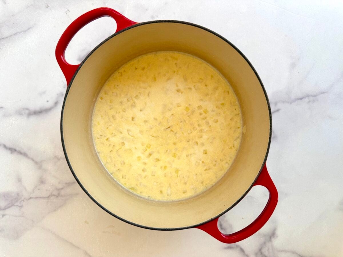 A red enameled cast iron pot containing a creamy yellow liquid with diced vegetables.