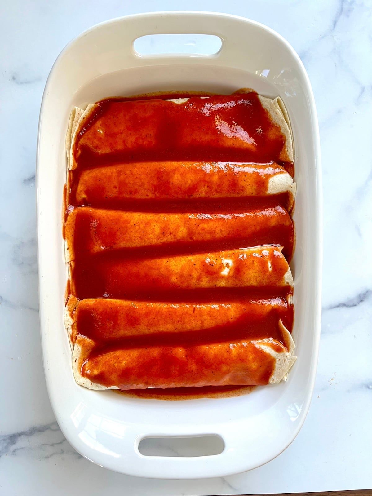 Enchiladas in baking dish topped with enchilada sauce.