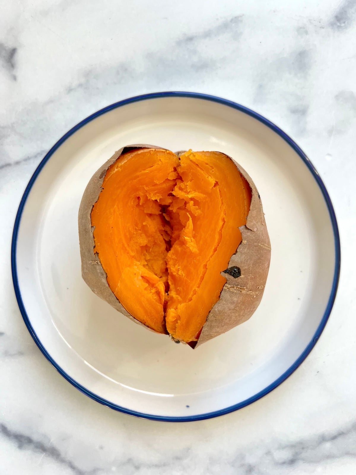 Baked sweet potato sliced in half on a plate.