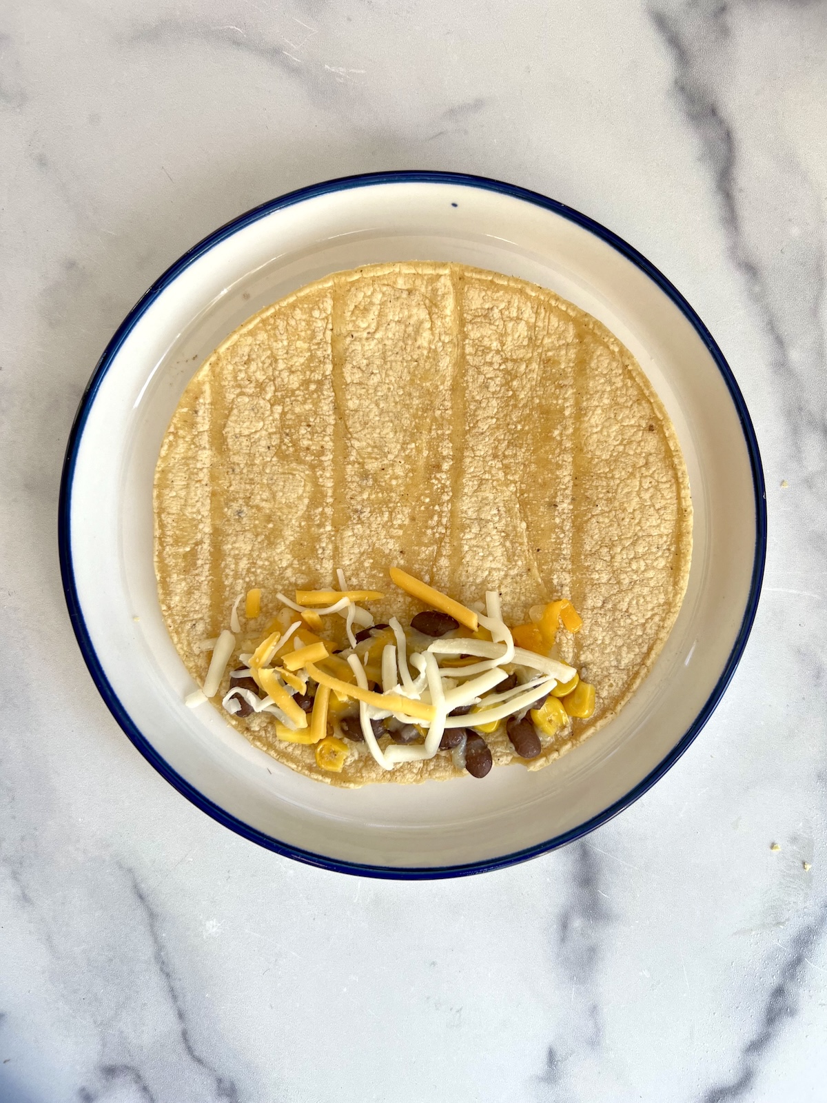 Corn tortilla with filling on one end ready to be rolled up.