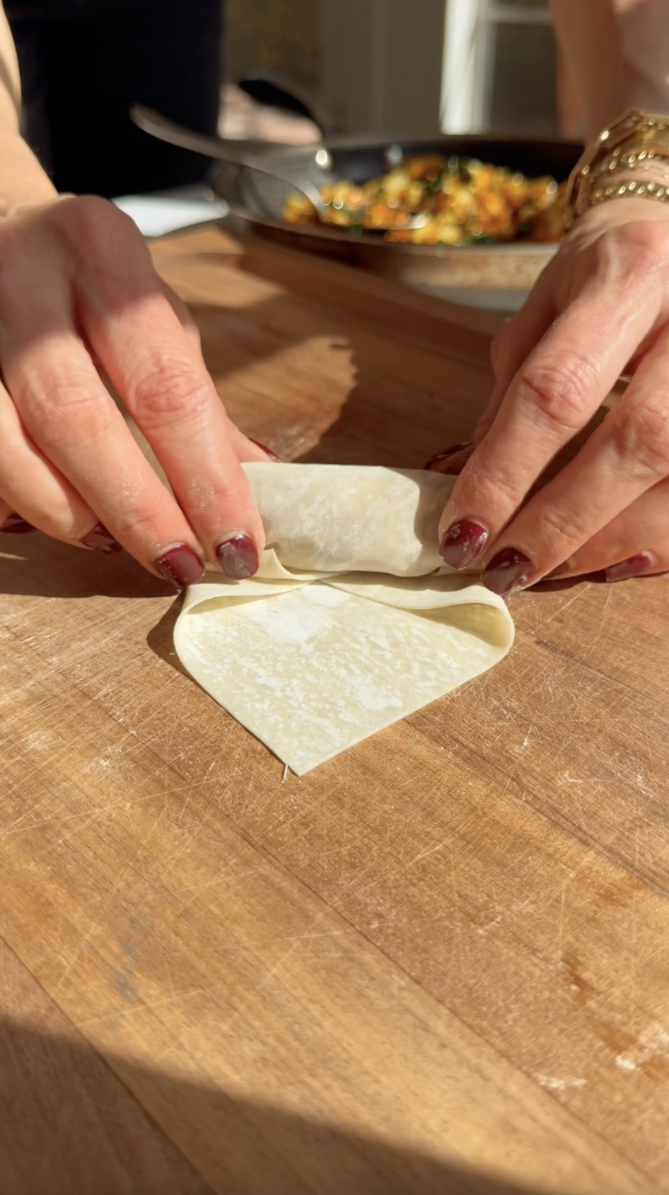 Rolling spring rolls on wooden cutting board.