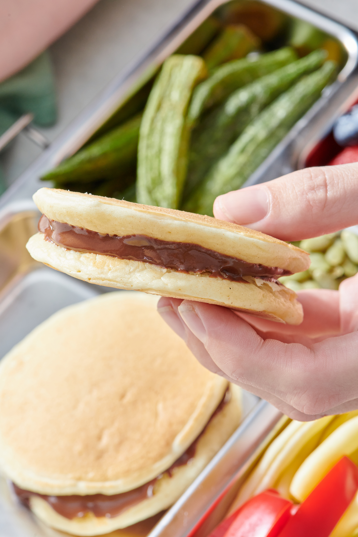 Hand holding chocolate sunbutter pancake sandwich.